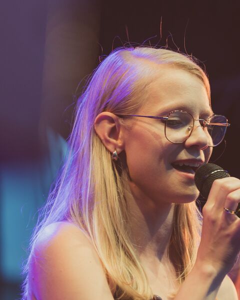 Dorota Wolniewicz śpiewa do mikrofonu na scenie, w fioletowym świetle.